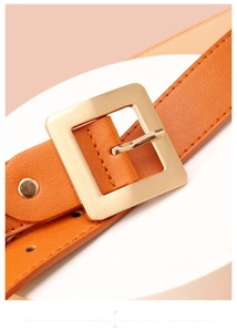 Detail of bright orange faux leather belt with a matte gold square metal buckle