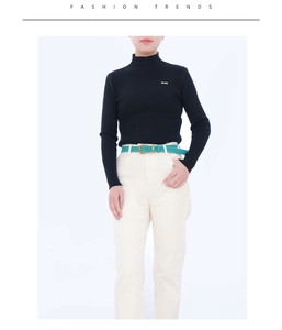 Close-up of a green leather belt with a gold buckle on white trousers and black sweater
