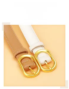 Close-up of slim PU leather belts in light brown and cream with matte gold oval buckles