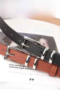 Close-up of black and brown minimalist belts with silver square buckles and stitching