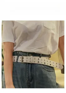 Dettaglio cintura punk bianca con borchie a stella e occhielli su jeans blu