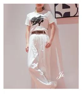 Dettaglio di una cintura punk in pelle marrone scuro con rivetti a stella su pantaloni bianchi