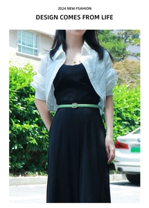 Detail of slim bright green leather belt with oval gold metal buckle worn on black dress