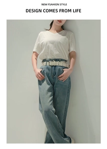 Dettaglio di una cintura bianca con borchie a stella punk su jeans blu a vita alta