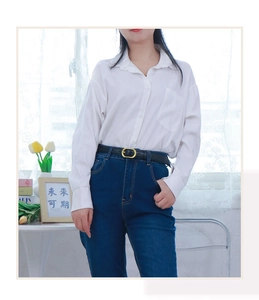 Close-up of minimalist black leather belt with gold oval buckle on blue high-waist jeans