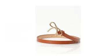 Dettaglio di una sottile cintura in pelle marrone con fibbia a fiocco dorata su sfondo bianco