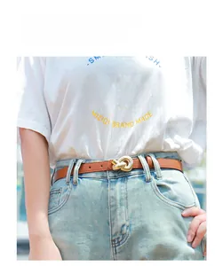 Detail of a brown leather belt with a gold metal knot buckle worn on light blue jeans