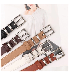 Detail of five slim faux leather belts with square silver buckles in assorted neutral colors