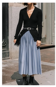 Detail of a black leather belt with a square buckle on a pleated light blue satin skirt