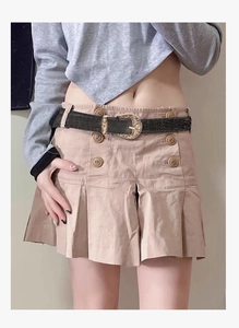 Detail of vintage carved brown leather belt on an apricot pleated mini skirt with buttons