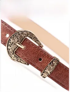 Macro shot of retro gold alloy buckle with intricate floral engraving on brown leather belt