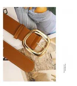 Close-up of caramel leather belt with a polished gold square buckle on a magazine background