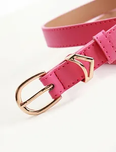 Dettaglio di una sottile cintura in pelle rosa con fibbia in metallo dorato a forma di V
