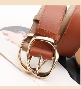 Detail of light gold irregular metal buckle and textured brown PU leather belt strap