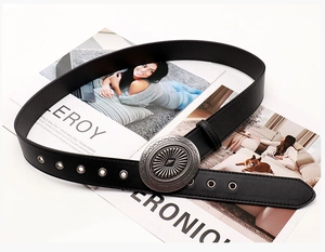Detailed view of the vintage black leather belt with silver eyelets and a round embossed buckle