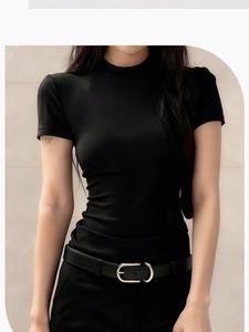 Detail of slim black leather belt with gold round buckle on women's jeans with black top