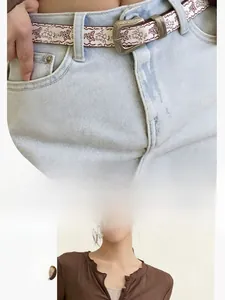 Détail de la ceinture vintage à fleurs et papillons avec boucle sur jean délavé