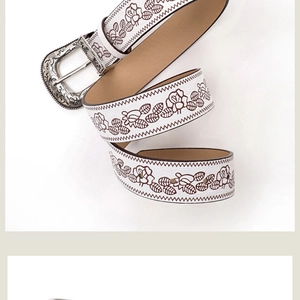 Detail of white vintage western belt with brown floral embossed patterns and silver metal buckle