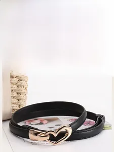 Détail d'une ceinture fine en similicuir noir avec une boucle dorée en forme de cœur brillant