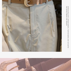 Detail of slim brown leather belt with textured gold buckle on khaki trousers