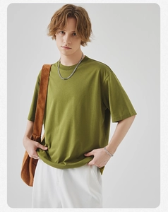 Detailed view of olive green cotton T-shirt paired with white trousers and brown crossbody bag