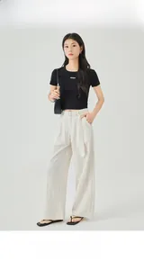 Dettaglio dei pantaloni beige a gamba larga a vita alta con cintura nera e crop top