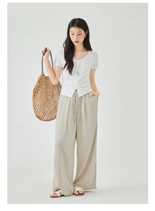 Detailed close-up of a white V-neck pleated top and beige wide-leg linen trousers