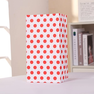 Gros plan d'un sac cadeau en papier blanc à pois rouges avec un bord supérieur dentelé