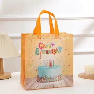 Yellow non-woven birthday gift bag with cake print and orange handles in warm setting