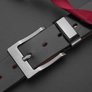 Detail of black leather belt with brushed metal pin buckle and red ribbon gift decor