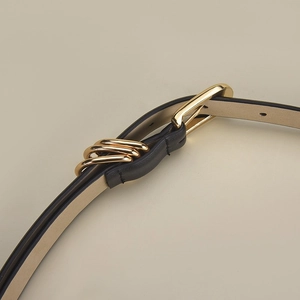 Dettaglio macro della cintura sottile in pelle nera con elegante fibbia a triplo anello
