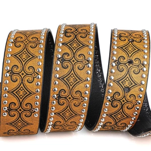 Macro view of vintage western leather belt featuring embossed floral vine patterns and silver studs