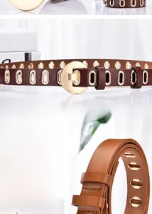 Détail d'une ceinture en cuir marron caramel avec œillets dorés et boucle ronde en métal