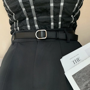 Detail of slim black waist belt with silver D-ring buckle on tailored trousers