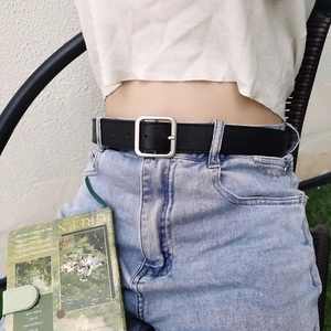Close-up of minimalist black leather belt with matte silver square buckle on waist