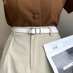 Detail of white litchi leather skinny belt with matte silver D-ring buckle on trousers