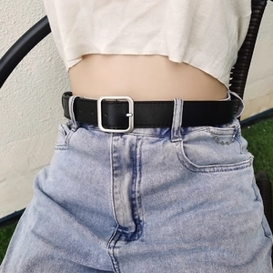 Detail of minimalist black leather belt with silver square pin buckle on denim jeans