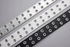 Close-up of double-eyelet punk belts in black, white, and silver faux leather textures