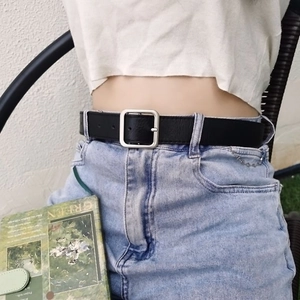 Women's black leather belt with silver square buckle worn on casual pants with accessories