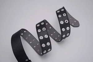 Detailed view of black punk style double grommet belt with silver metal eyelets and stitching