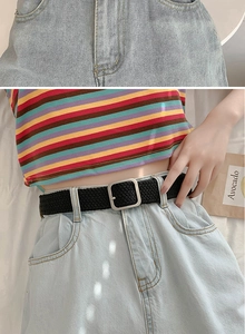 Detalle de cinturón trenzado negro elástico con hebilla plateada y vaqueros denim