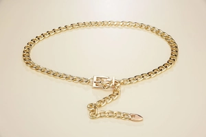 Close-up of golden metallic chain belt featuring large links and a heart-shaped pendant