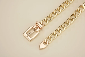 Detailed close-up of a glossy gold metal chain belt featuring a sleek rectangular pin buckle