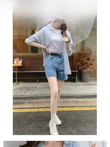 Gros plan d'un short en jean taille haute porté avec une chemise bleue et un t-shirt blanc