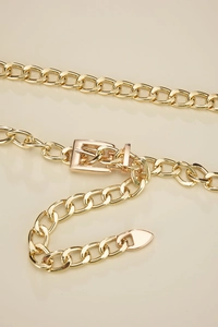 Detail of gold chain belt featuring a polished square pin buckle and heart-shaped metal tip