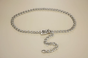Detail view of silver chain belt with pin buckle and heart pendant on beige surface