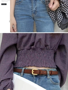 Détail d'une fine ceinture en cuir marron avec boucle dorée sur un jean bleu clair