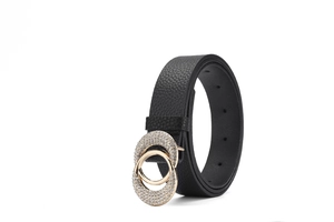 Détail d'une ceinture noire en cuir grainé avec boucle double cercle dorée sertie de strass