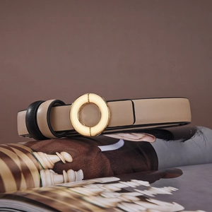 Detailed view of beige leather slim belt with a polished gold round buckle on a magazine