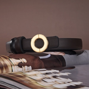 Detail of a minimalist gold circular buckle on a brown leather belt over magazines